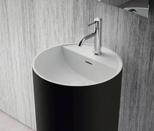 Black cylindrical freestanding sink with white basin against a wooden wall.