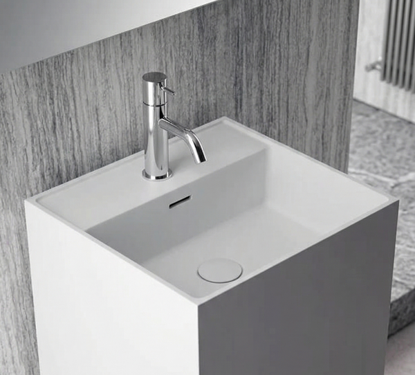 White pedestal sink with silver faucet against a gray tiled wall.