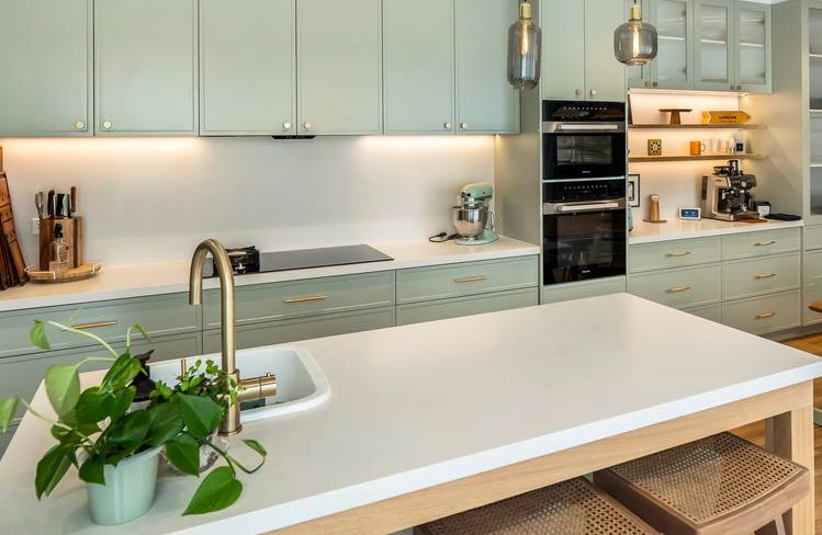 Modern kitchen with light green cabinets, white countertops, and stainless steel appliances.
