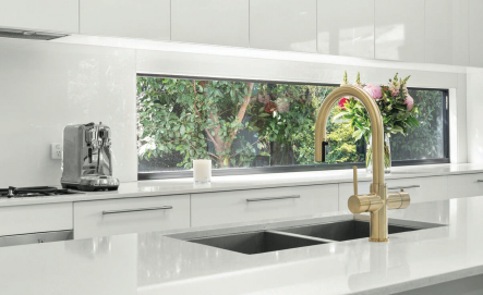 Modern kitchen with a gold faucet and white countertops.